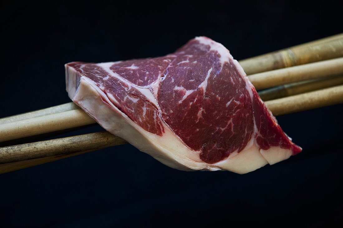 A Wagyu beef ribeye steak on bamboo sticks