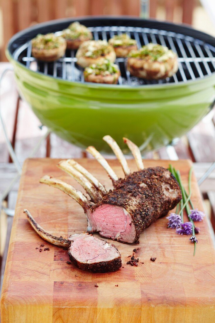 Grilled lamb rack with a barbecue in the background