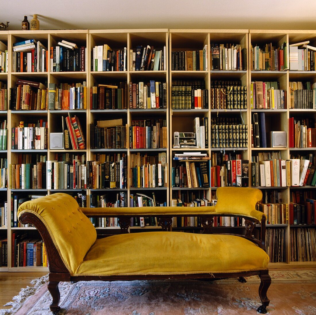 Antique divan upholstered in yellow velvet in front of a modern library wall