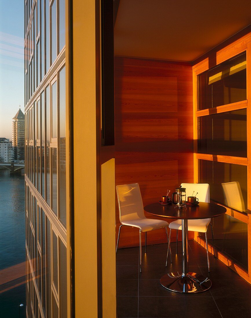 Warm, sunny light in a modern wood paneled loggia with bistro table and white chairs