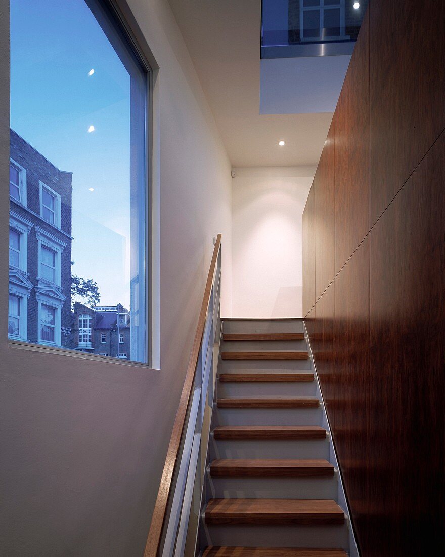 Stairs in front of wood paneled wall in designer style and large picture window with a view of the neighboring house