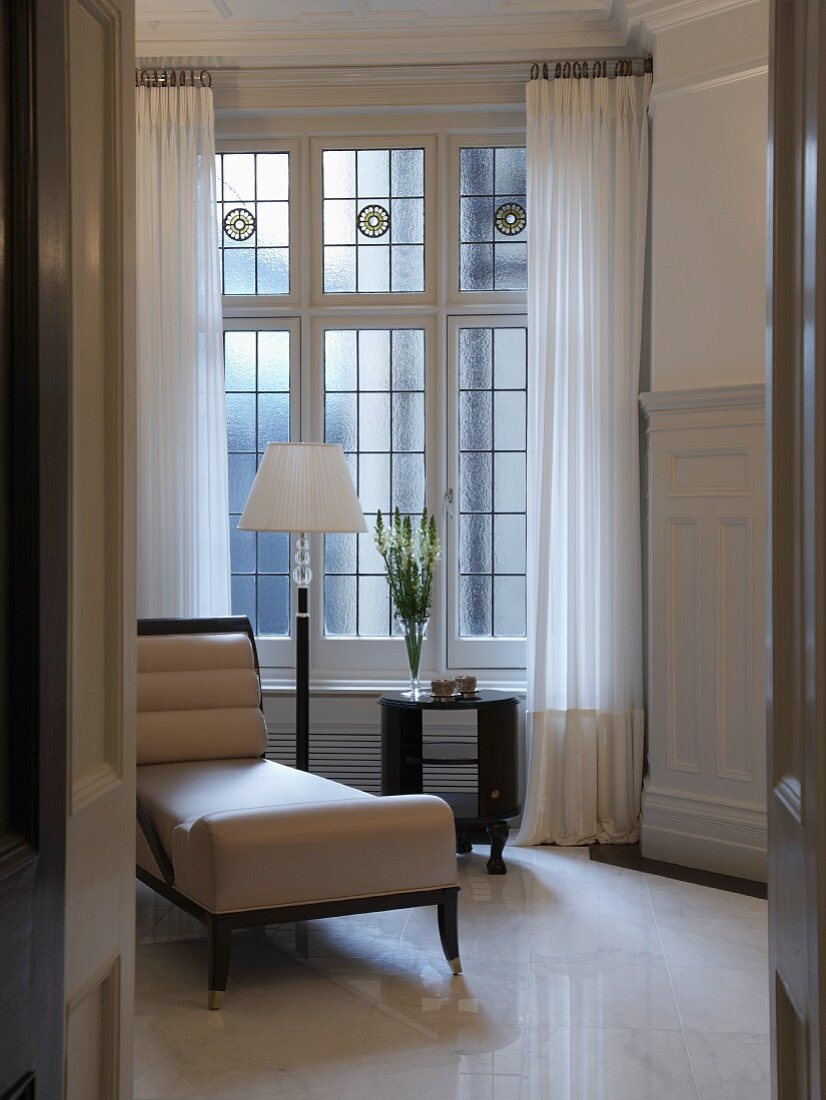 View through an open door of a chaise lounge upholstered in white leather in Art Deco style in front of leaded windows