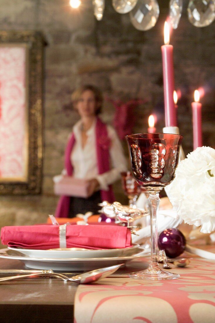 A table laid for Christmas dinner decorated in pink and a woman in the background with a present