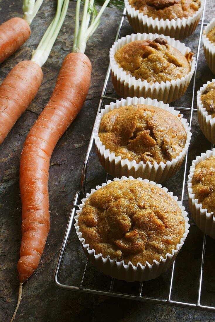 Carrot muffins on a wire rack with carrots next to them