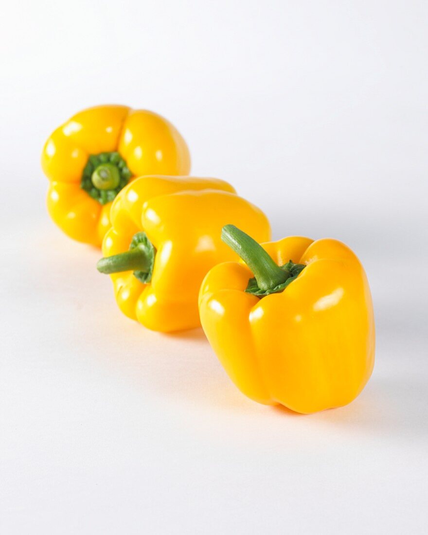 Three yellow peppers on a white surface