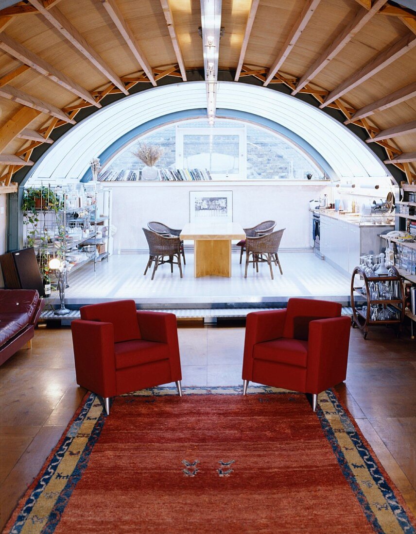 Red armchairs on a platform with dining area in an open room under a barrel roof