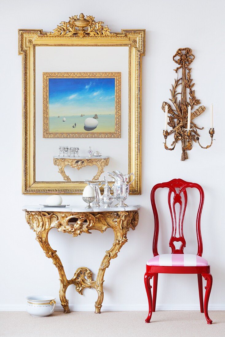 Rococo wall table and a red chair with a picture in a gold frame and a wall candle holder above