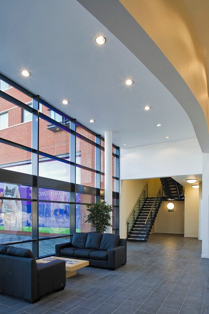 Spacious reception hall with leather furniture under ceiling spotlights and a bank of windows