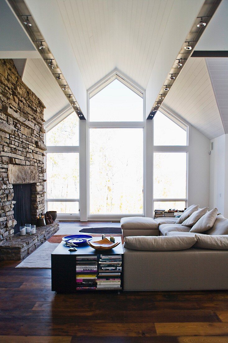 Living room with sofa and rustic, open fireplace in front of ceiling high gable windows