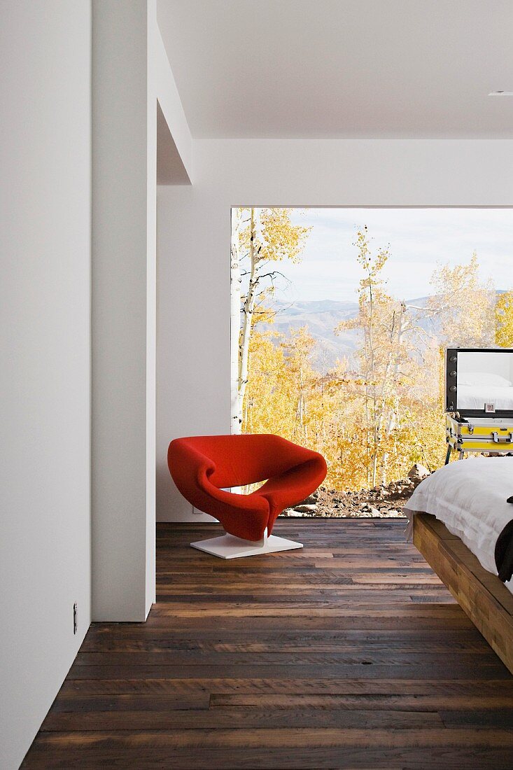 Roter Designersesssel vor raumhohem Fenster mit Landschaftsblick im Schlafzimmer