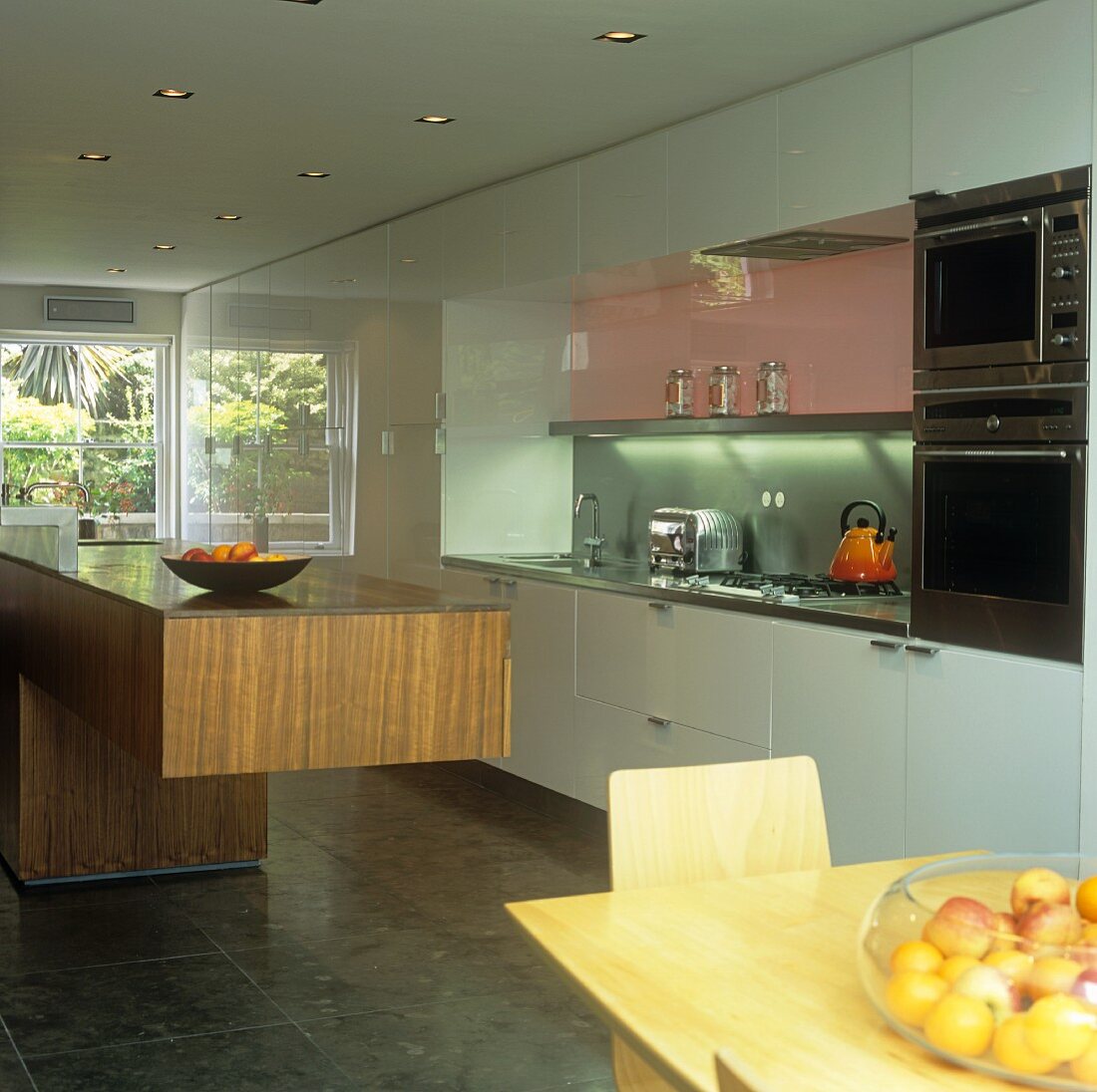 A dining area in front of a free-standing walnut kitchen counter in an open-plan kitchen with white cupboards