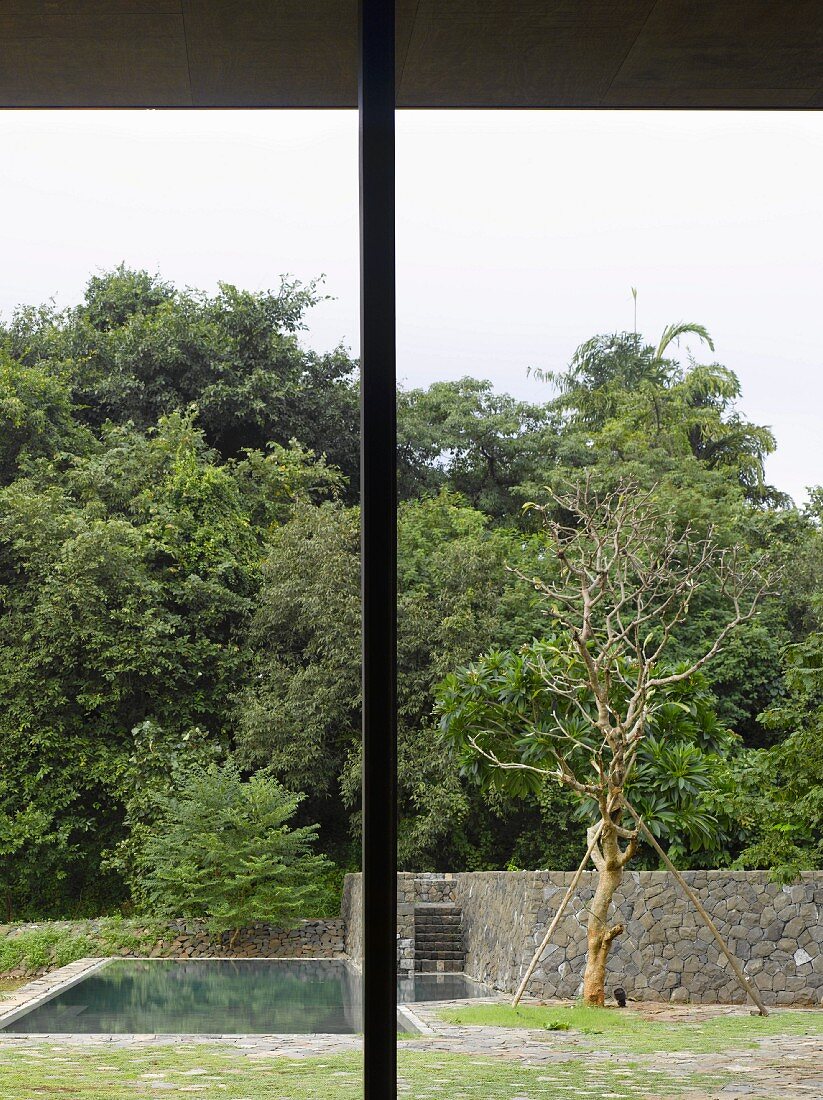 Metal terrace support and view of garden with pool and stone wall