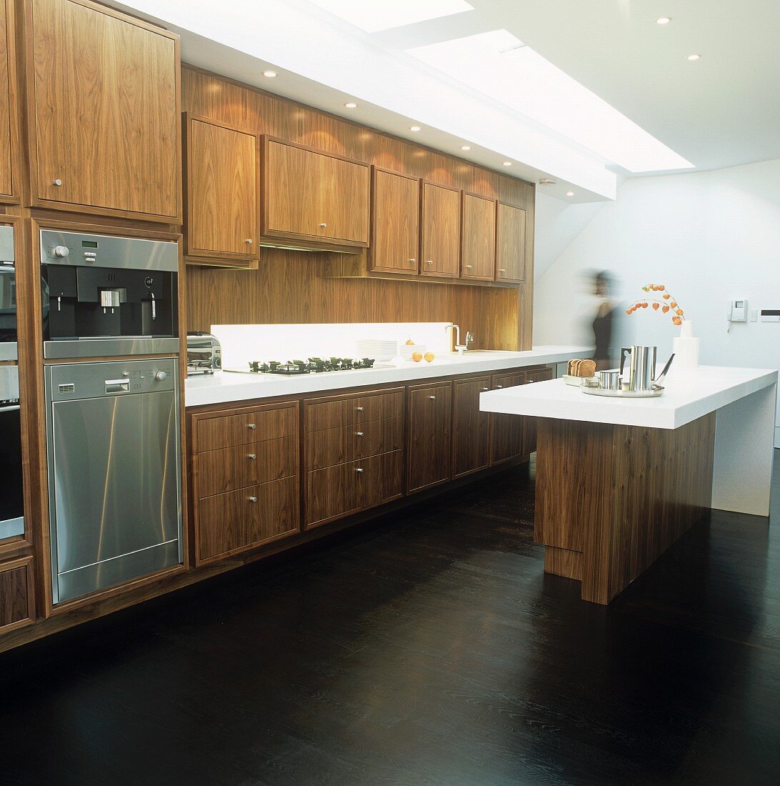 An open-plan, fitted kitchen with wooden cupboards and a bar with a white surface