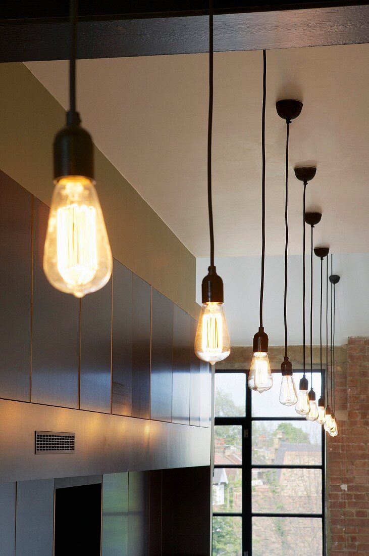 Pendant lamps with large, teardrop-shaped light bulbs in a high-ceilinged room with traditional factory windows