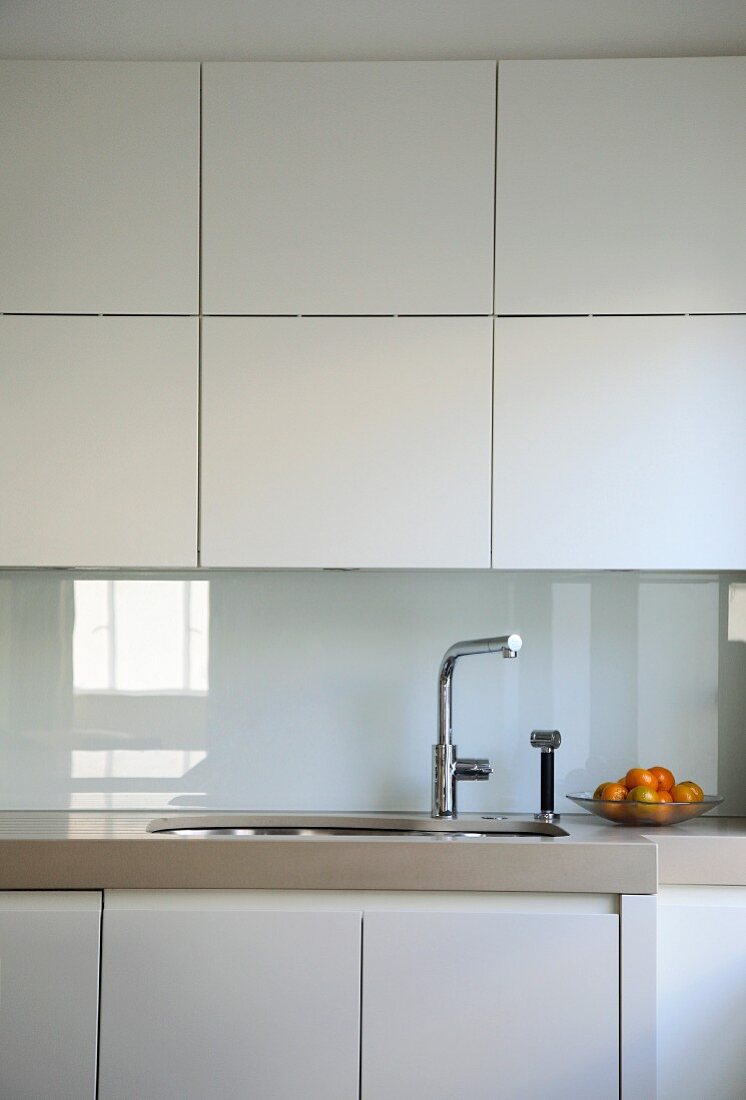 White fitted kitchen with flat fronts and reflective splash guard in white glass