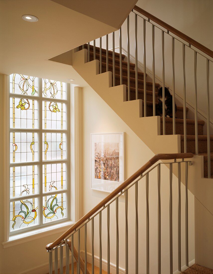 Plain, modern apartment staircase with stepped, white facings in front of window with floral, stained, leaded glass