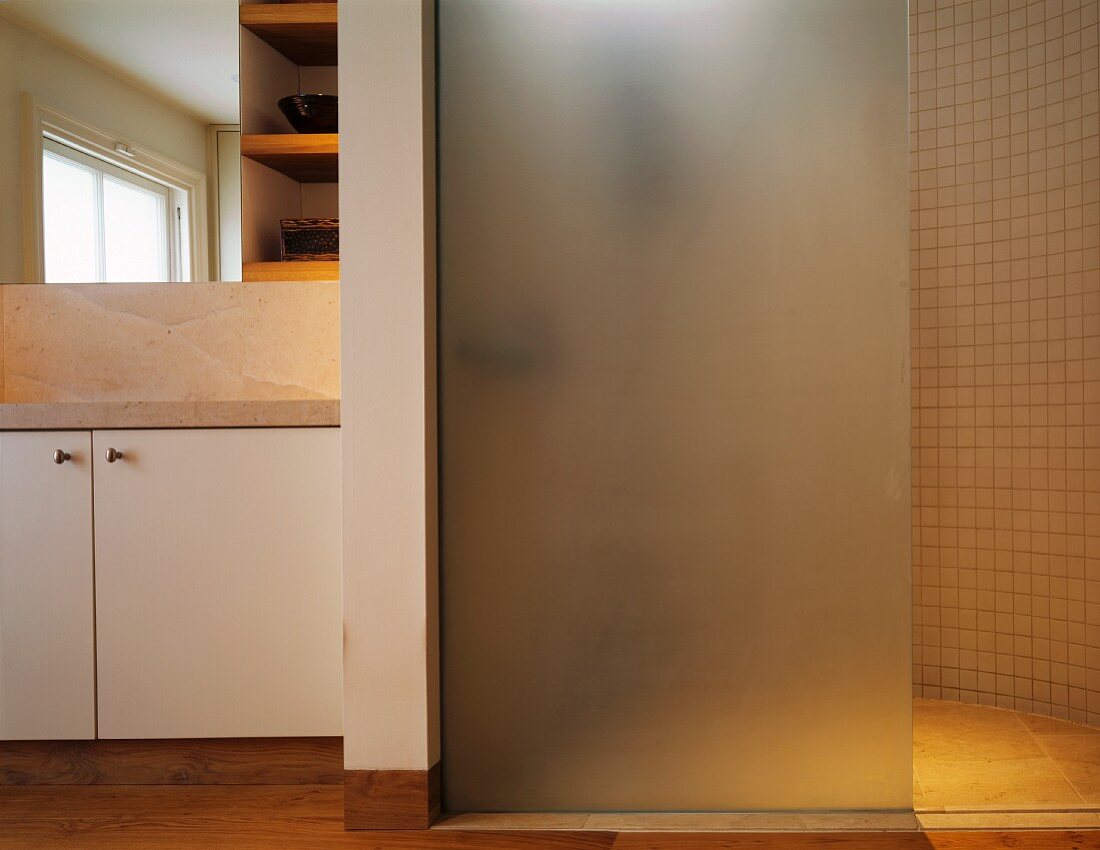 Frosted glass shower partition in bathroom with stone tiles and wooden flooring