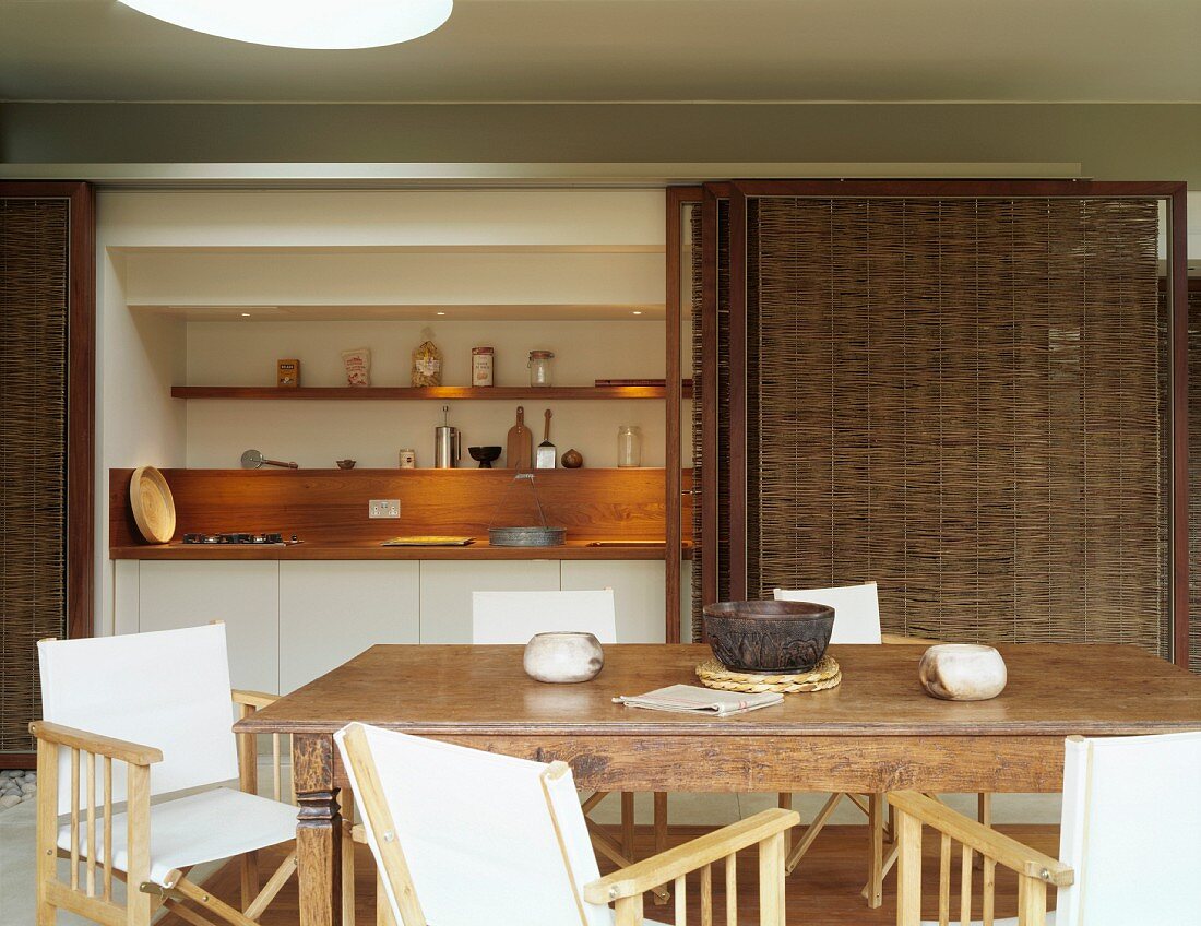 Antique wooden table and director's chairs in front of niche with small kitchen counter and bamboo sliding doors