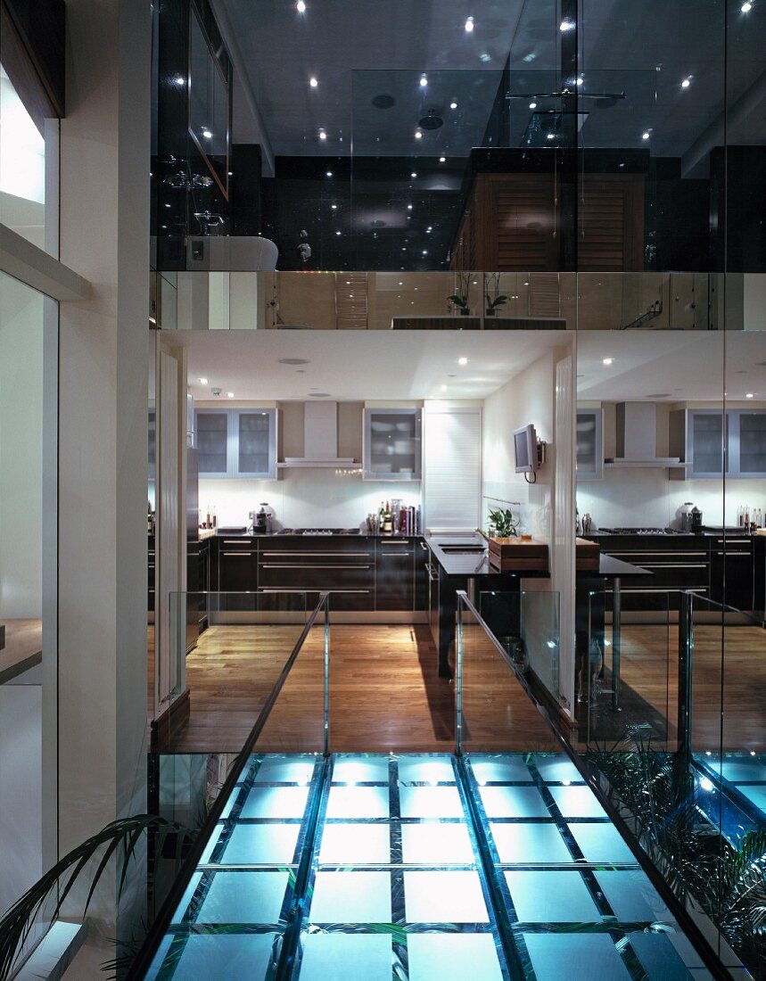 Bridge of illuminated glass bricks with view of rooms between reflective glass panels in English house