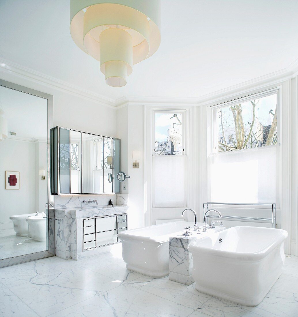 Vintage bathtubs on marble floor with designer ceiling light in spacious, traditional bathroom with bay window