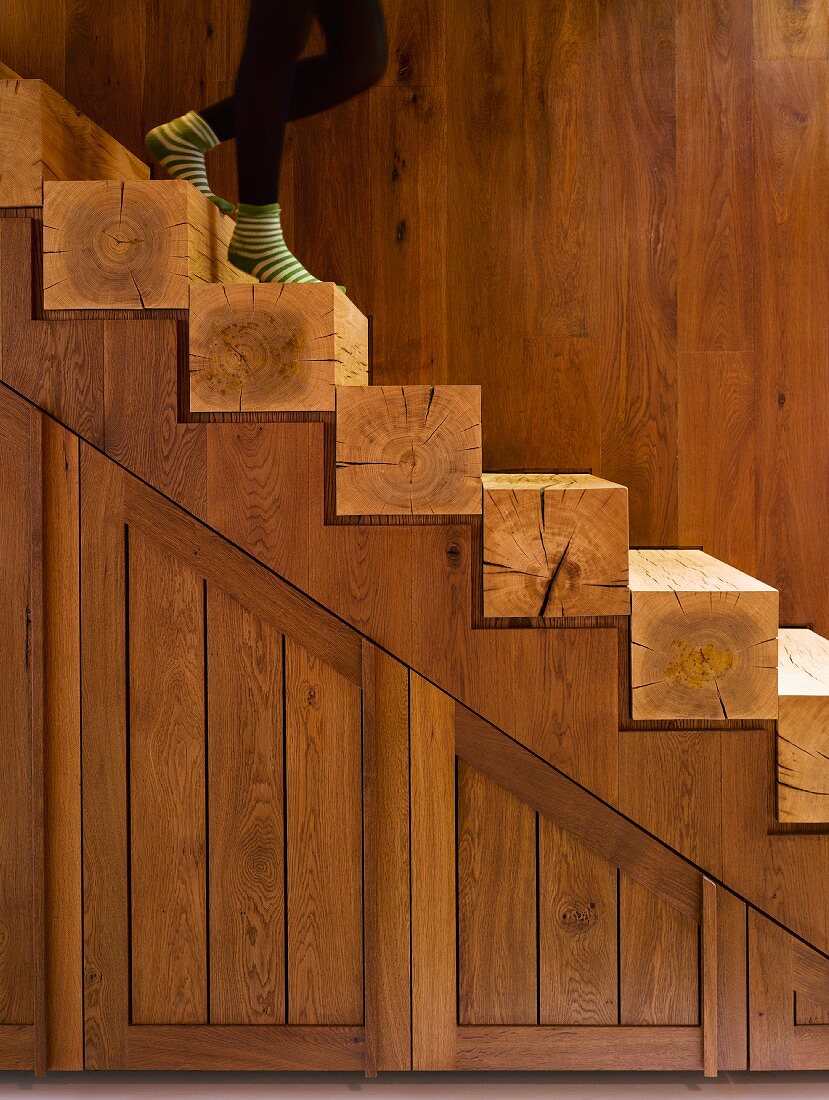 Partially visible person on open-plan wooden staircase with square timber steps in front of wooden wall