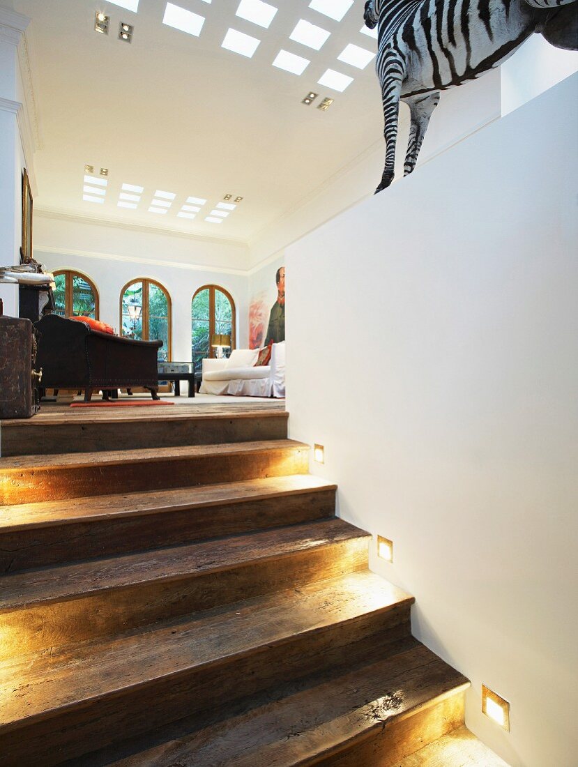 Recessed spotlights on rustic wooden steps leading to open-plan living room