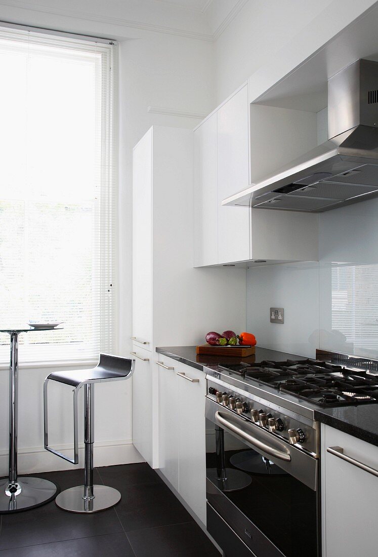 Moderne Küche mit weissen Fronten und Barhocker vor Bistrotisch am Fenster