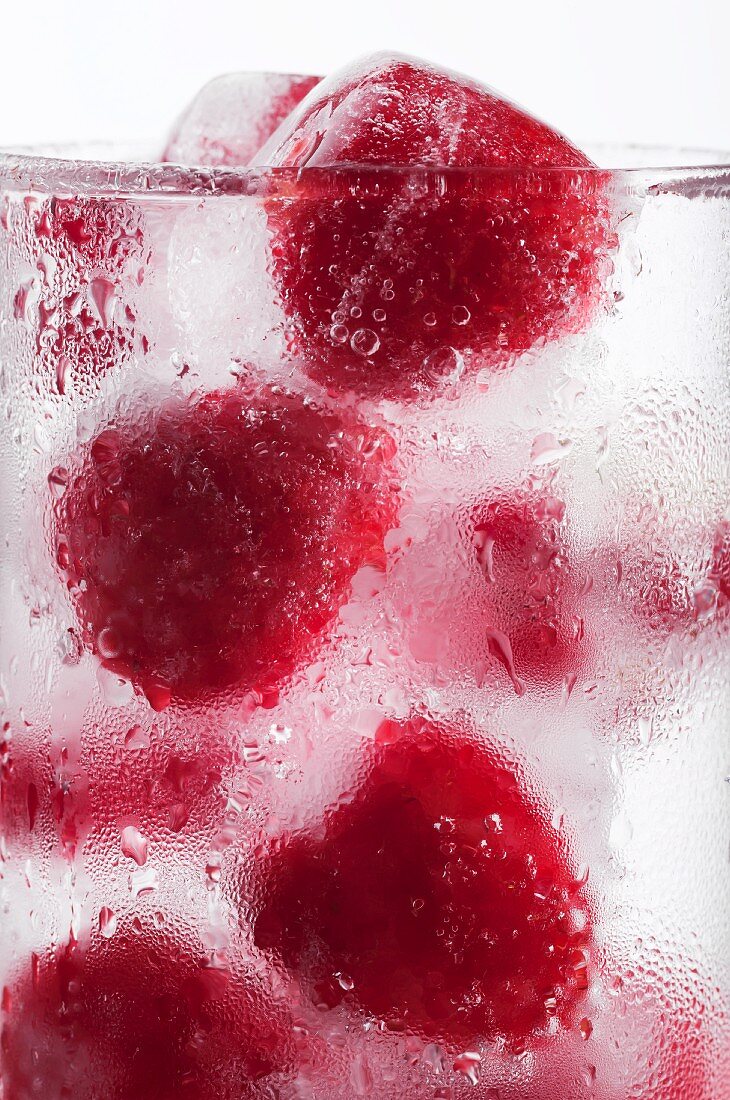 A glass of water with raspberry ice cubes