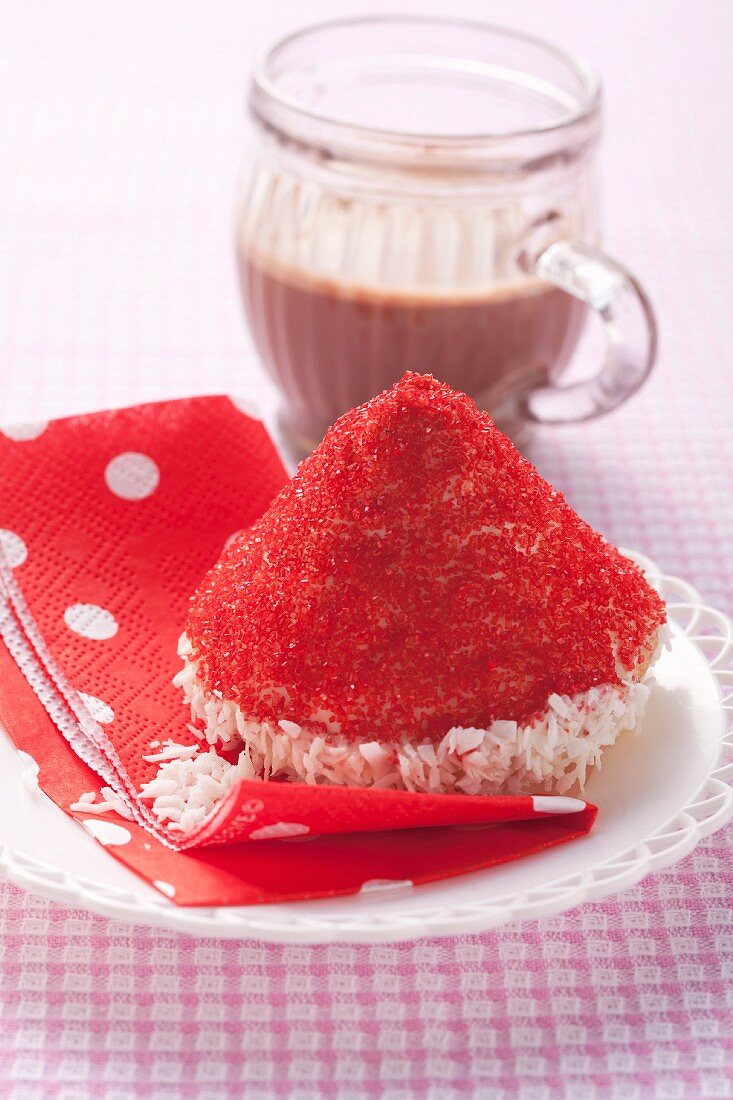 A cake topped with a red hat made of desiccated coconut and sugar sprinkles