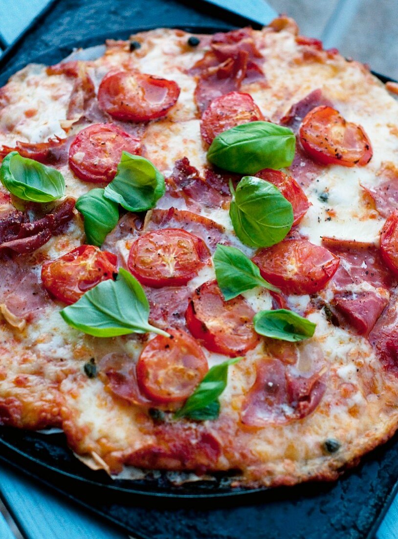 A pizza topped with fresh tomatoes, ham and basil