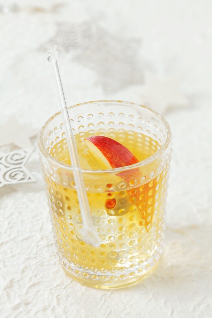 A vodka and apple juice drink with a slice of apple and an olive