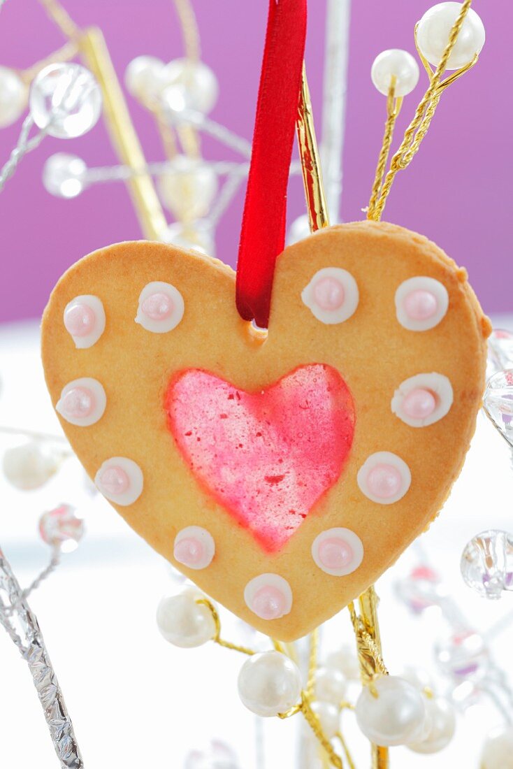 A heart-shaped Christmas biscuit with jam hanging on a twig