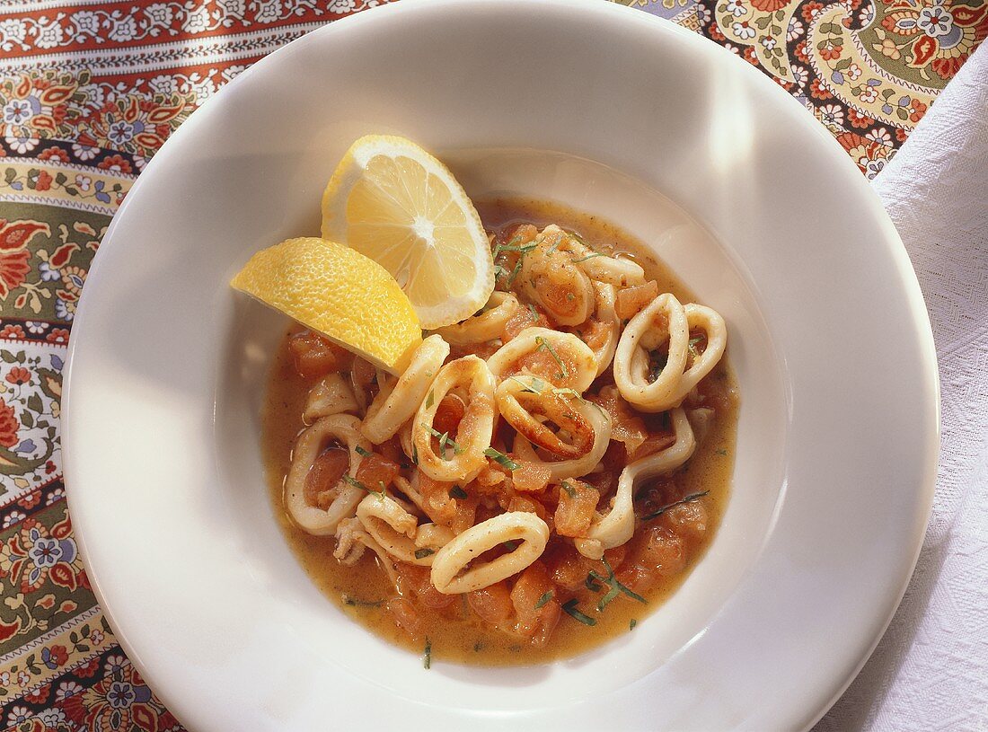 Braised squid in tomato broth with lemon wedges