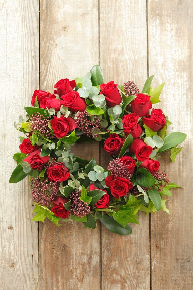 A bunch of eucalyptus, roses, ivy and skimmia hanging on a wooden wall