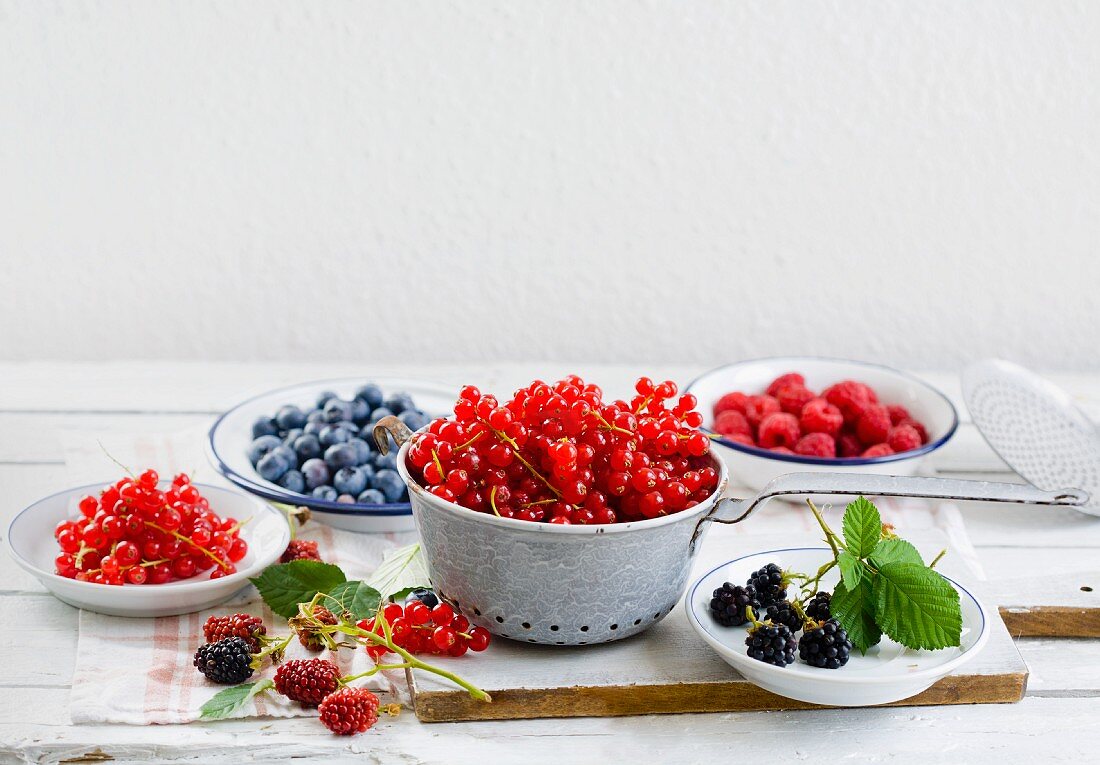 Verschiedene Beeren auf kleinen Tellern und im Küchensieb