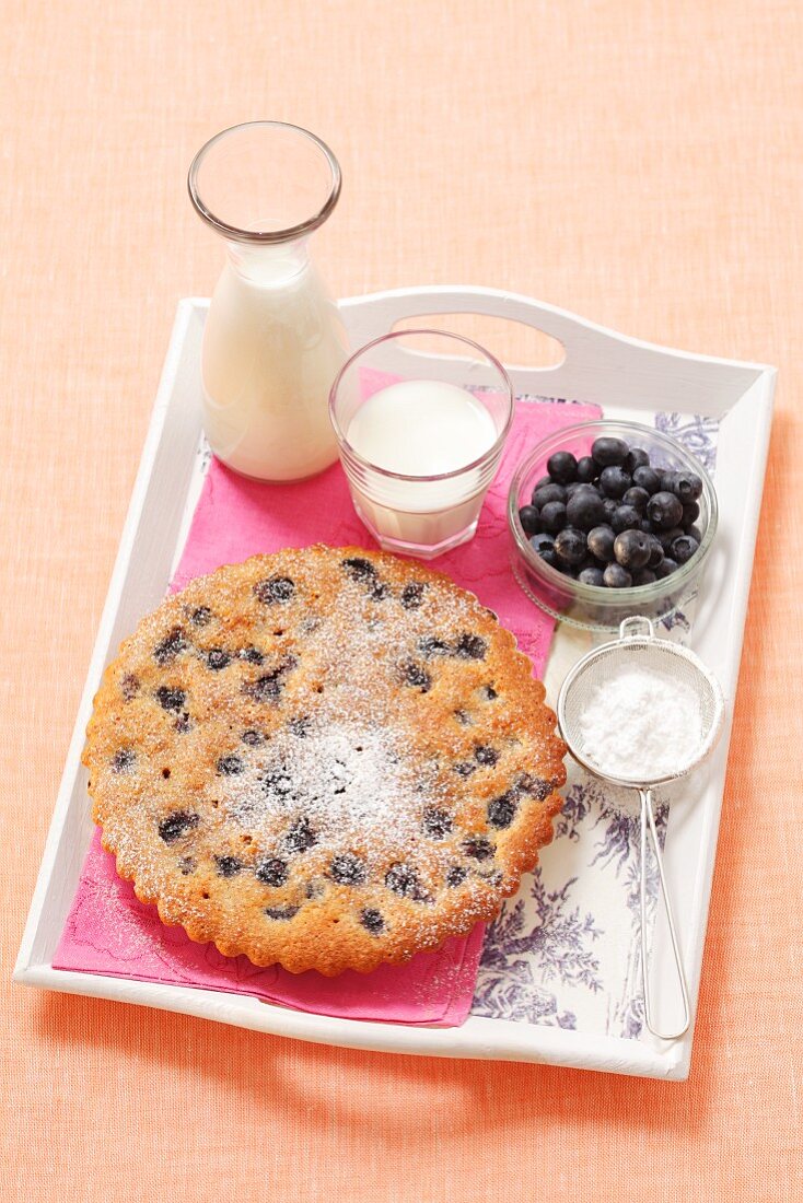 An almond tart with blueberries and icing sugar on a tray