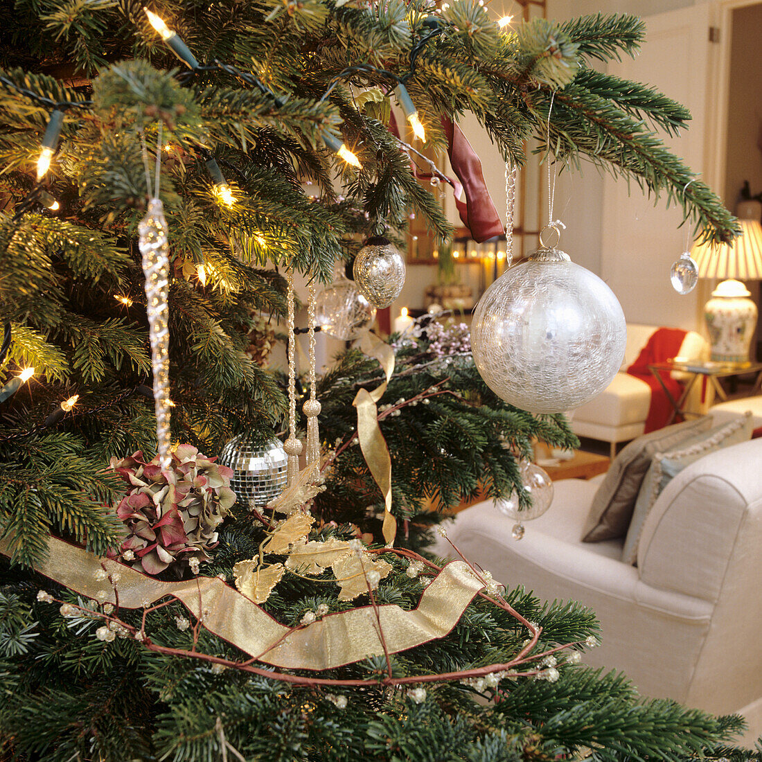 Weihnachtlich geschmückter Tannenbaum mit Lichterkette und silbernen Kugeln im Wohnzimmer