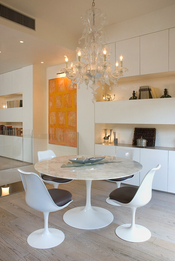 Round marble table with white designer chairs and chandelier in the modern dining room