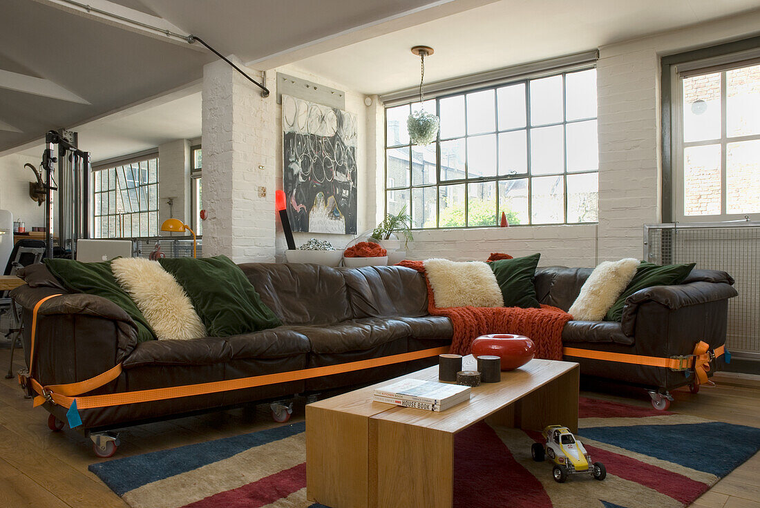 Loft-Wohnzimmer mit Ledercouch, bunten Kissen und Industriefenstern