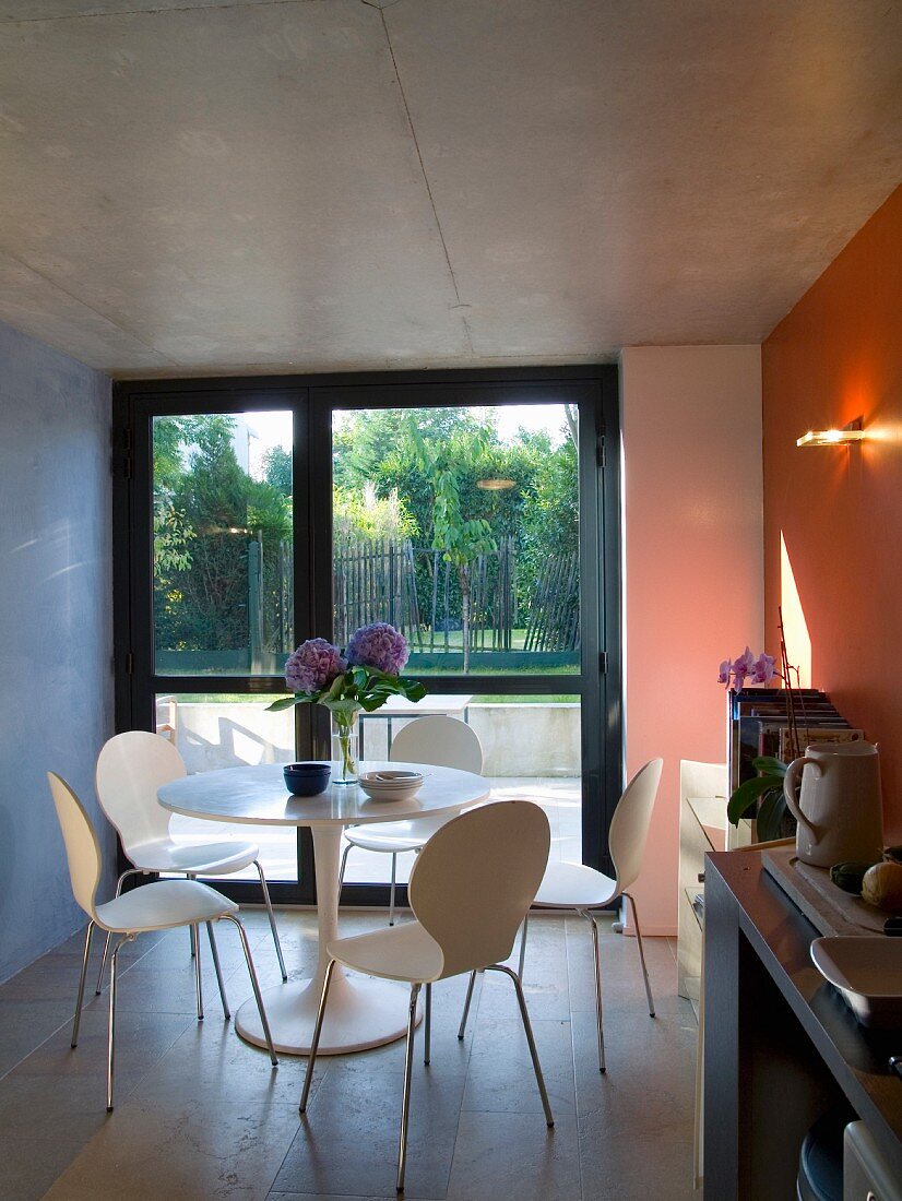 Dining table with white chairs in front of floor-to-ceiling windows in contemporary building