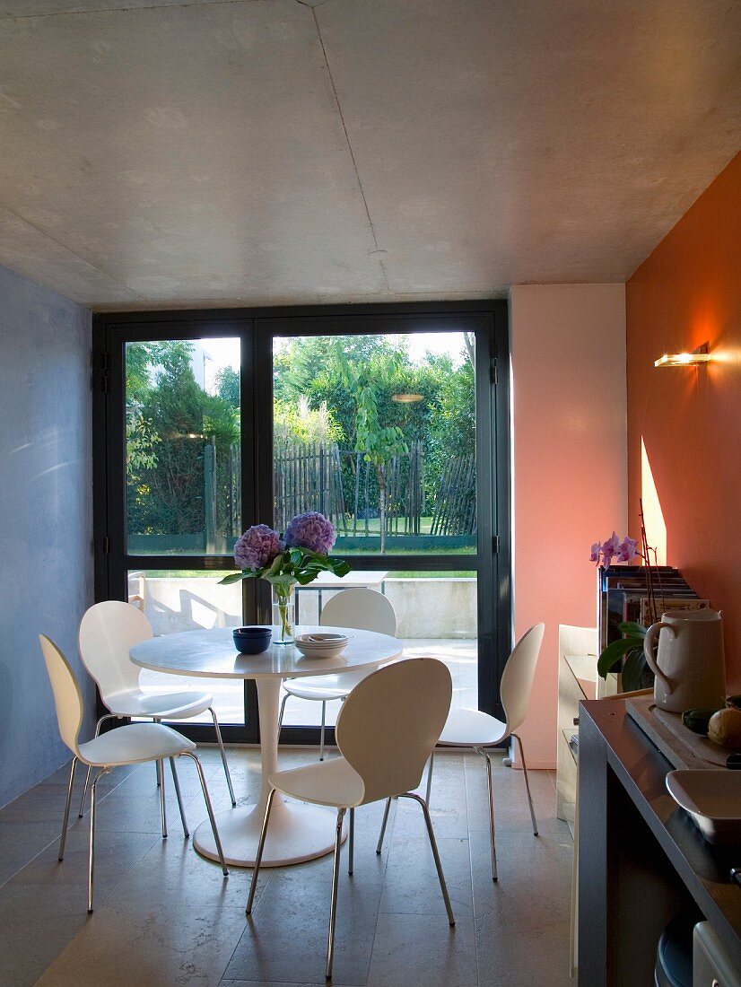 Esstisch mit weissen Stühlen vor raumhohen Fenstern in zeitgenössischer Architektur