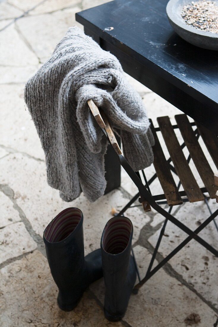 Pullover auf Stuhllehne und Gummistiefel auf Terrasse