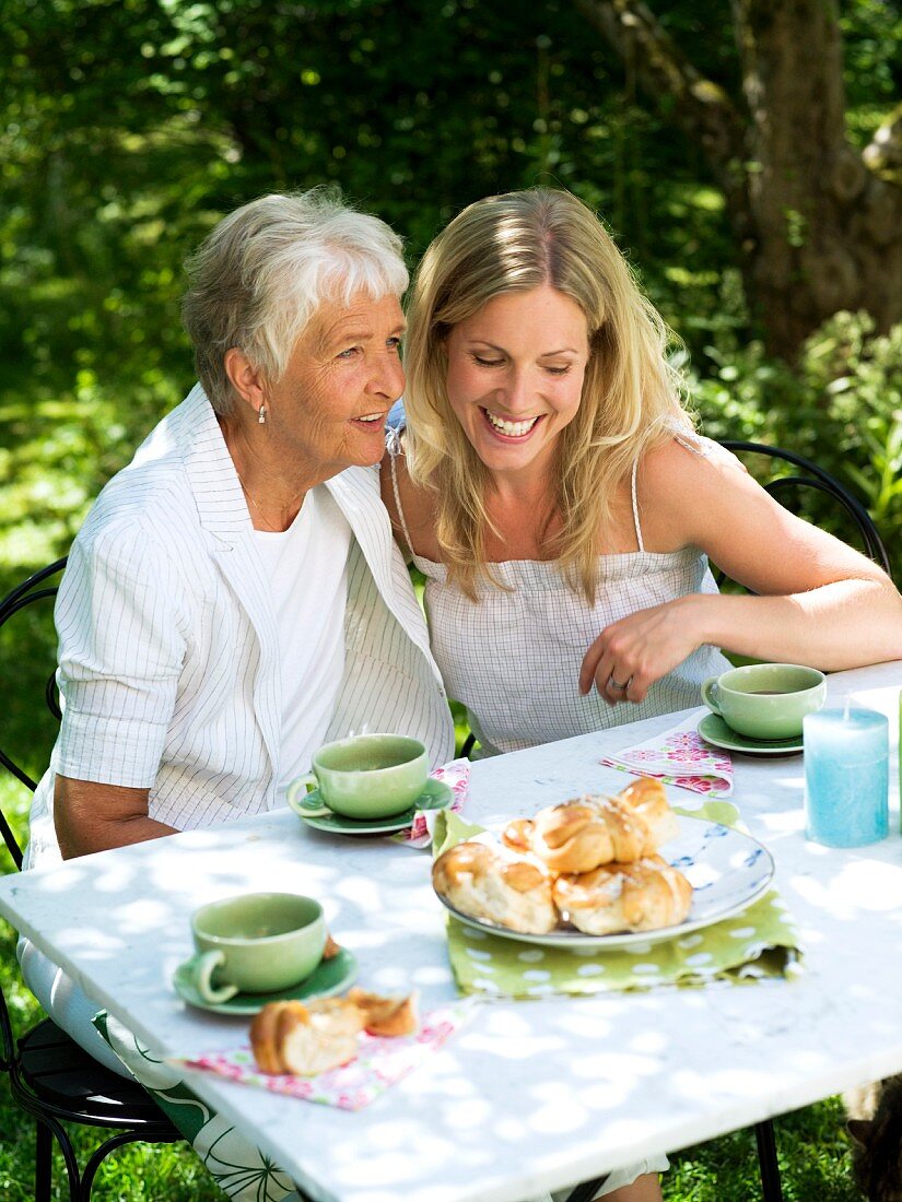Ältere und junge Frau trinken Kaffee im Garten