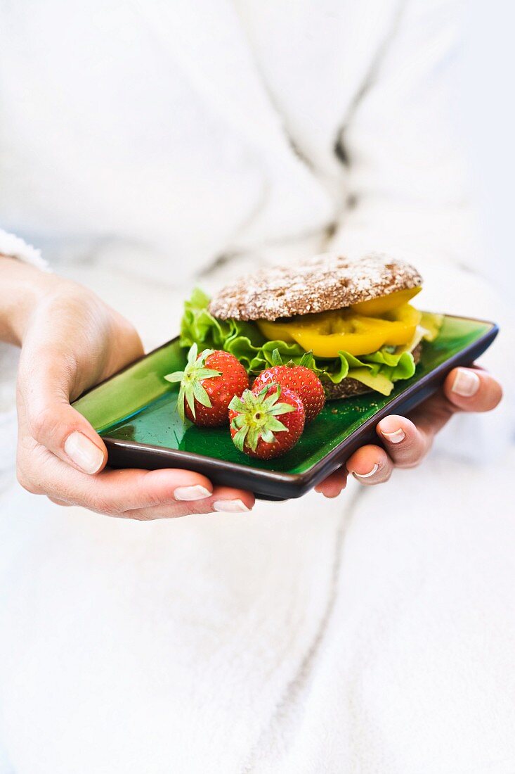 A woman holding a pepper and strawberry sandwich