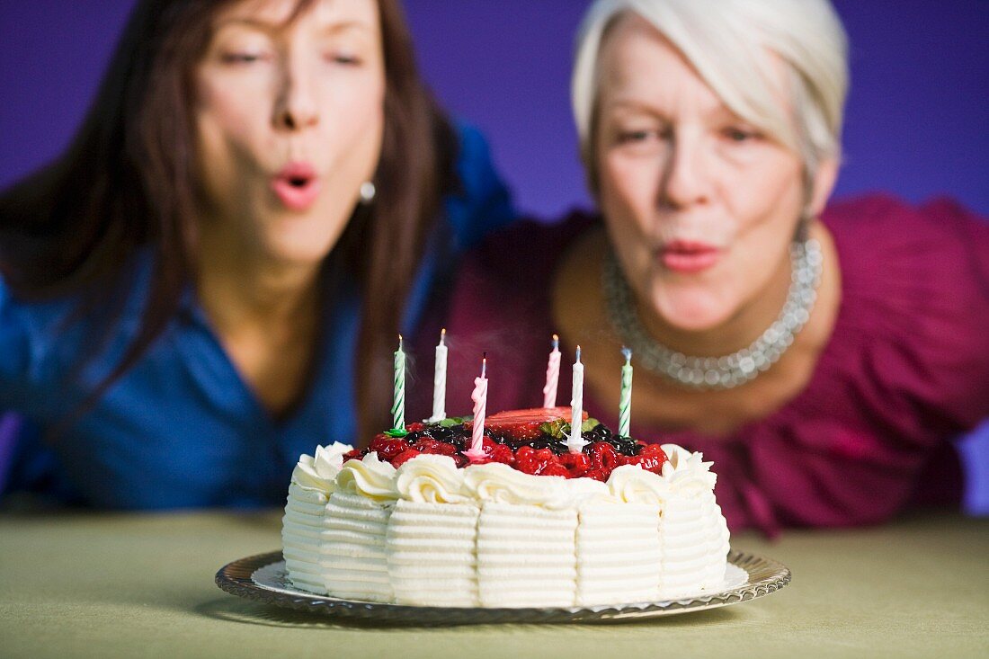 Two women blowing out candles on a birthday cake