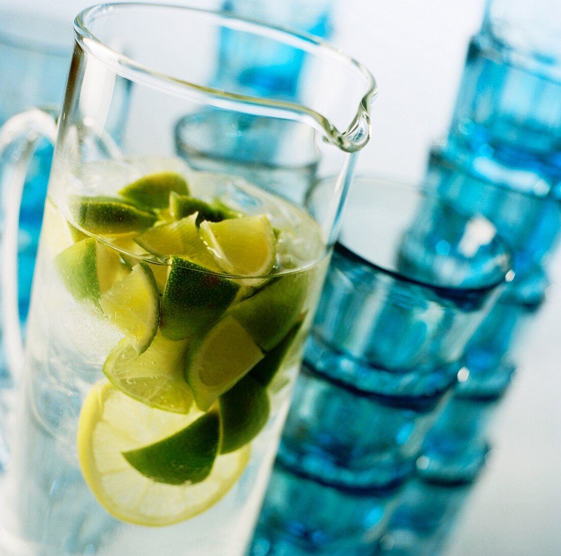 A glass jug of water with limes