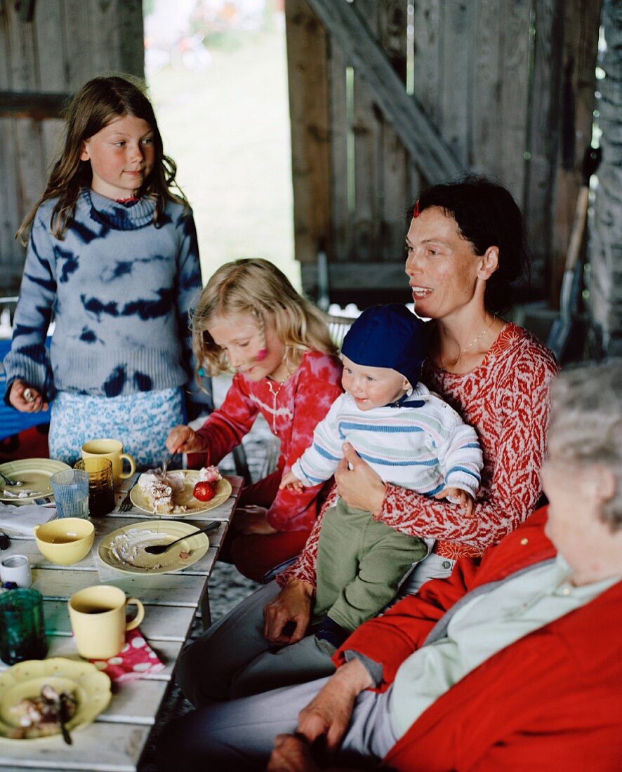 Zwei Frauen und drei Kinder essen Kuchen in einer Scheune