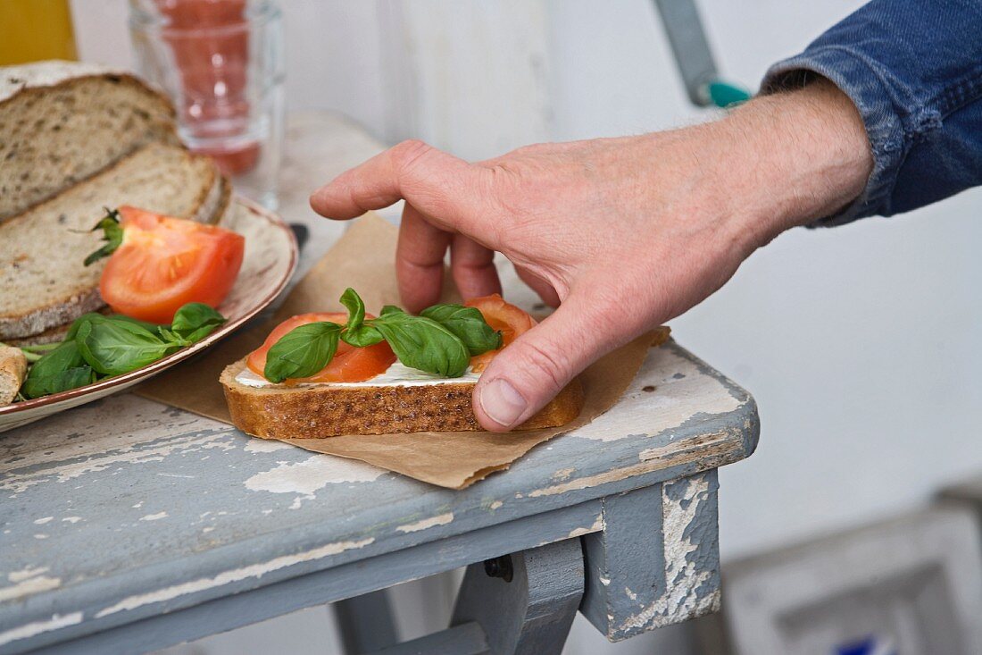 A hand taking a slice of bread topped with tomatoes and basil