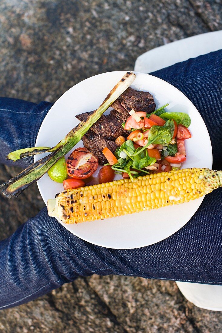 Grilled beef steak with salad and a corn cob