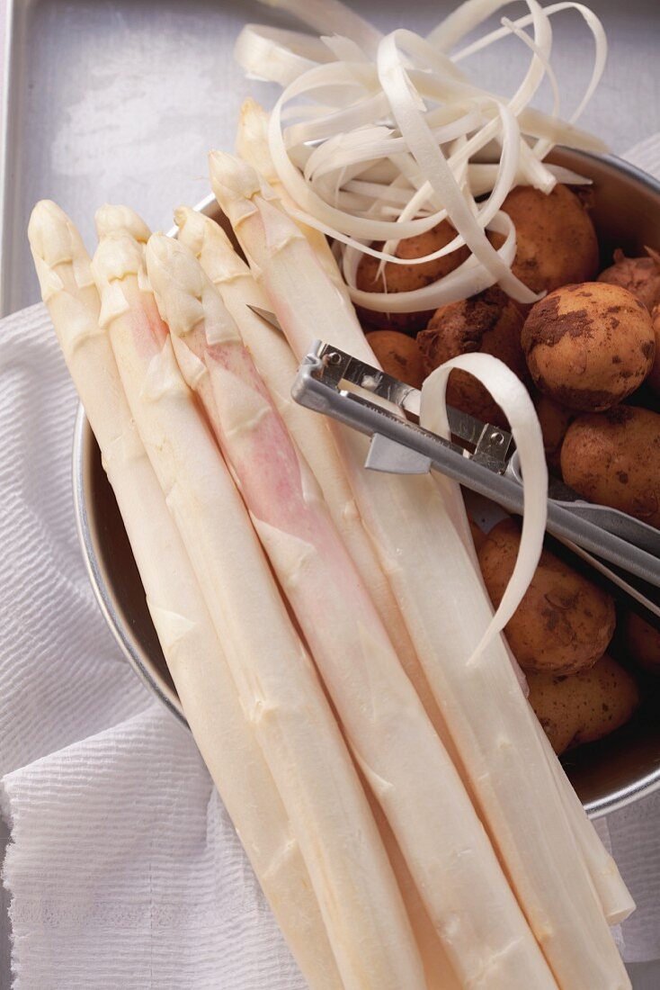 White asparagus with a peeler on top of potatoes